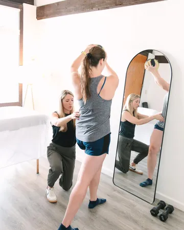 A She PT therapist coaching a patient through a standing exercise at the mirror
