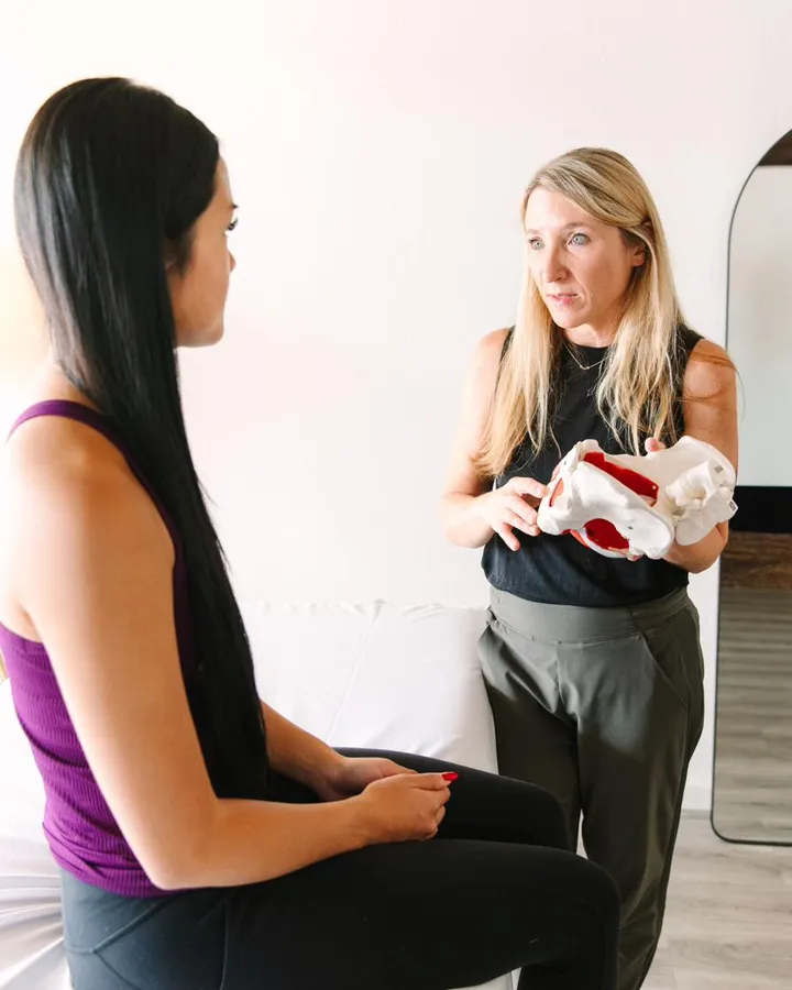 A She PT therapist showing a patient a pelvis model during an evaluation in a private treatment room